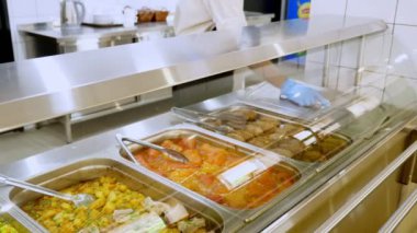 Yemek pişirmek. Yakın plan. Garson koruyucu eldivenlerle konteynırları yemeklerle, cam vitrinlerin arkasında, self servis kafeteryasında ya da açık büfede açar. Sağlıklı yemek. Gönüllülük ve yardım
