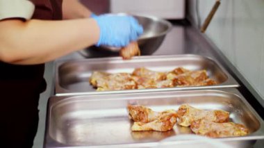 Yakın plan. Mutfak işçisi, koruyucu eldivenlerle, fırında pişirmek için çiğ tavuk bacağı serer. Sağlıklı yemek. Gönüllü olmak ve yardım. Covid-19 'dan sonra tekrar açılıyor. güvenlik kavramı.