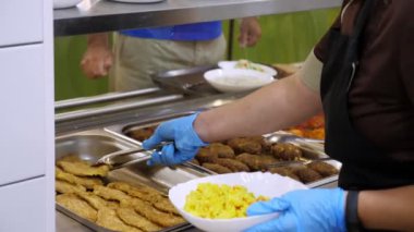 Yemek pişirmek. Yakın plan. Garson, koruyucu eldivenlerle, self-servis kafeteryasında ya da açık büfede müşterilere yemek hazırlıyor. Covid-19 'dan sonra tekrar açılıyor. Güvenlik kavramı. sağlıklı gıda.