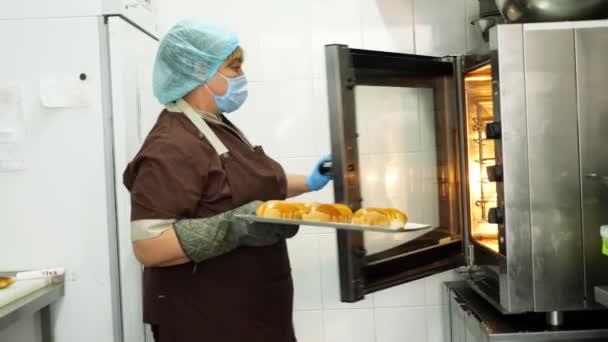 Kochen. Bäckerei. Die Köchin holt in Schutzhandschuhen frisches Gebäck aus dem Ofen. gesunde Ernährung. Wiedereröffnung nach Covid-19. Sicherheitskonzept. Freiwilligenarbeit und Wohltätigkeit. — Stockvideo