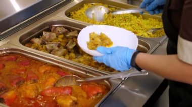 Yemek pişirmek. Yakın plan. Garson, koruyucu eldivenlerle, self-servis kafeteryasında ya da açık büfede müşterilere yemek hazırlıyor. Covid-19 'dan sonra tekrar açılıyor. Güvenlik kavramı. sağlıklı gıda.