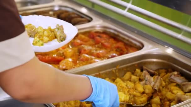 Cuisiner. Gros plan. serveuse, dans des gants de protection, met de la nourriture dans l'assiette pour le client à la cafétéria libre-service ou restaurant buffet. réouverture après covid-19. concept de sécurité. aliments santé. — Video