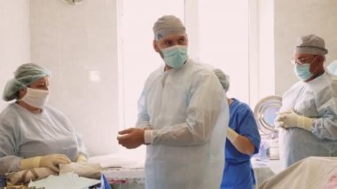 Hemşire, cerrahın koruyucu kıyafet giymesine yardım ediyor. Operasyon için hazırlık. İlaç. Hastanede ameliyat ve canlandırma. covid-19 salgını