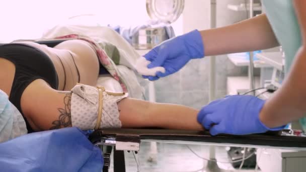 Zbliżenie. Pacjentka leży na stole operacyjnym. Pielęgniarka leczy jej ramię środkiem antyseptycznym przed włożeniem cewnika. medycyny. operacja i resuscytacja w szpitalu. pandemia wywołana przez kovid-19 — Wideo stockowe