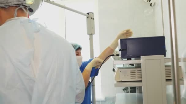 Une infirmière, dans des gants et un masque médicaux, surveille un dispositif spécifique pendant une opération chirurgicale. chirurgie et réanimation à l'hôpital. équipement médical — Video