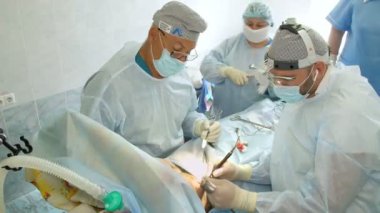 Cerrah, kadın hastaya lazer kullanarak göğüs altından bir kesik atar. Ona başka bir doktor yardım ediyor. Göğüs büyütme estetiği. Mammaplasti. Göğüs kanseri