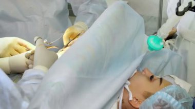 Yakın plan. Cerrah ve asistanı silikon implantları yerleştirdikten sonra meme bezlerinin altındaki kesikleri dikerler. Göğüs büyütme estetiği. Mammaplasti. Göğüs kanseri.