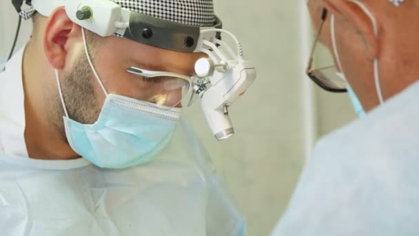 Portrét chirurga v lékařské masce a chirurgických loupách, provádí operaci na operačním sále nemocnice. — Stock video