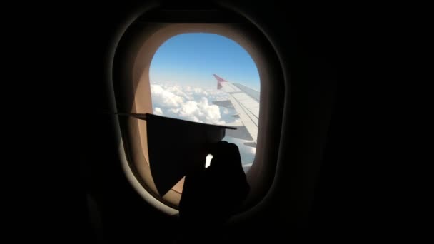 Zbliżenie. ciemna sylwetka dziecięcej dłoni z zabawką. Kid siedzi przy oknie samolotu i bawi się papierową zabawką na tle okna samolotu, iluminator . — Wideo stockowe