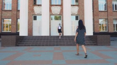 Anne okul bahçesinde kızıyla tanışır. Okul kızı ve kadın, ikisi de koruyucu maskeler takıyor. 19. salgından sonra okula döndüm. Covid-19 saatinde selamlar.