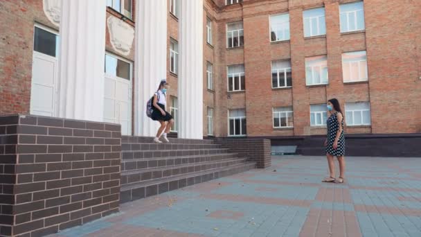 Mamá conoce a su hija de la escuela en el patio de la escuela. colegiala, con mochila, y la mujer, ambos en máscaras protectoras. Regreso a la escuela después del brote de covid19. — Vídeos de Stock