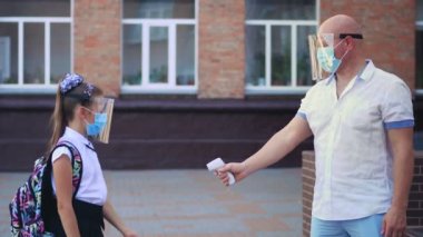 Güvenlik görevlisi, dijital medikal elektronik termometre kullanarak okul binasına girmeden önce kızın vücut ısısını ölçüyor. Covid19 salgınından sonra okula döndüm.
