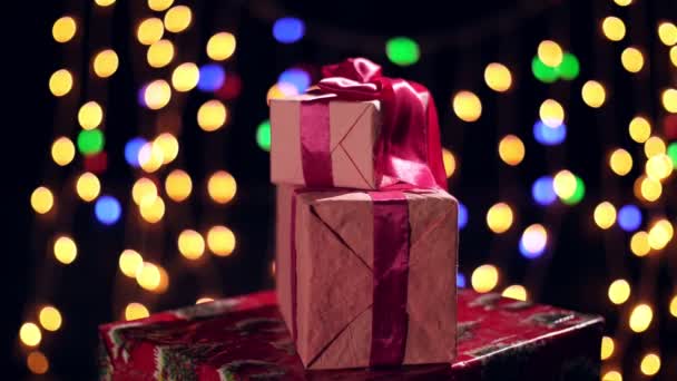 Pięknie zapakowane prezenty z różowymi wstążkami. prezentuje się na bokeh światła lub świecące girlandy tła. zbliżenie, obrót. Boże Narodzenie albo Nowy Rok. Koncepcja dobroczynności. świąteczna atmosfera. — Wideo stockowe