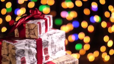 Kırmızı kurdeleli güzel paketlenmiş hediyeler. Bokeh ışıkları ya da parlak çelenkler hakkında sunumlar. Yakın çekim, rotasyon. Noel ya da yeni yıl. Yardım konsepti. Şenlikli atmosfer.