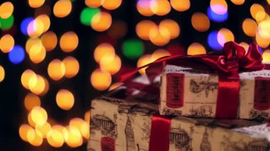 Kırmızı kurdeleli güzel paketlenmiş hediyeler. Bokeh ışıkları ya da parlak çelenkler hakkında sunumlar. Yakın çekim, rotasyon. Noel ya da yeni yıl. Yardım konsepti. Şenlikli atmosfer.