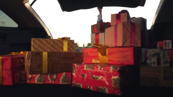 Gift boxes in the car. a woman unloads many beautifully wrapped, packed boxes, from car trunk. view from inside the car. donation, charity concept. delivery of gifts, parcels — Stock Video