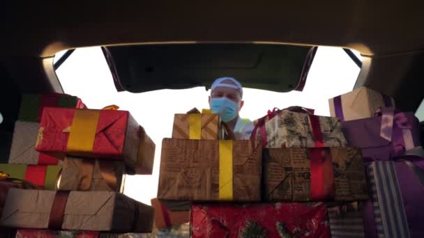 Lieferservice. Lieferant in Schutzmaske. Kurier entlädt Kisten. Geschenkboxen im Auto. schön verpackte Pakete. Blick aus dem Inneren des Autos. Spende, Charity oder Lieferkonzept. — Stockvideo