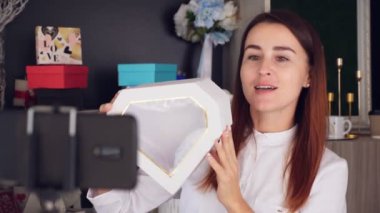 Tasarımcı hediye paketliyor. Çekici kadın dekoratör online yayın, konferans, video blogu, web sitesi, akıllı telefonun önünde duruyor. çevrimiçi çalış.