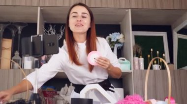 Tasarımcı hediye paketliyor. Çekici kadın dekoratör online yayın, konferans, video blogu, web sitesi, akıllı telefonun önünde duruyor. çevrimiçi çalış.