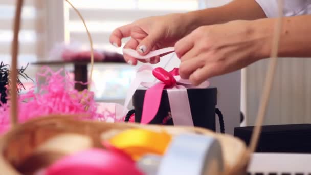 Regalos envolviendo primer plano. Diseñador de regalos y decoraciones decora, empaca una caja de regalo, ata un lazo de cintas de seda rosa — Vídeos de Stock