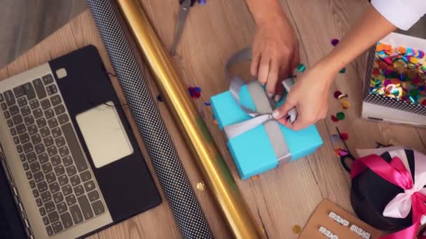 Geschenkverpackung aus nächster Nähe. Ansicht von oben. Designer von Geschenken und Dekorationen dekoriert, verpackt eine Geschenkbox, bindet eine Schleife mit Seidenband vor dem Laptop. Videoblog, Webinar. — Stockvideo