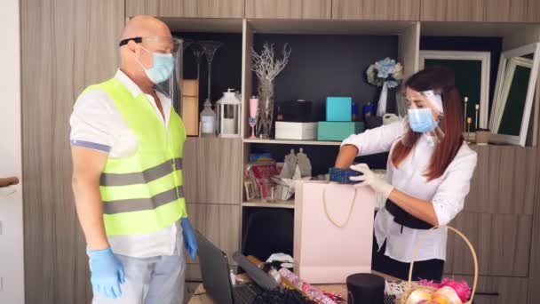 Lieferservice für Pakete, Geschenke. Kurier trägt Schutzmaske. Designer, in Maske, packt Geschenktüte. Hauszustellung aufgrund Coronavirus-Pandemie. Online-Verkauf, Online-Shopping. — Stockvideo