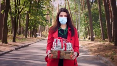 Paketli hediyeler. Koruyucu maskeli bir kadın elinde güzel paketlenmiş kutular tutuyor. Açık havada. Teslimat ya da bağış, bağış konsepti. Tatil için hediyeler