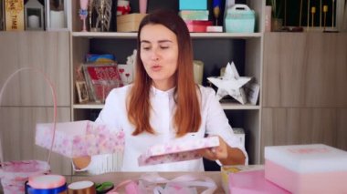 Hediyeler paketleniyor. Çekici bir kadın, hediye ve dekorasyon tasarımcısı çevrimiçi eğitim programları, video bloğunu kaydediyor, giyim kuşamını takıyor, akıllı telefonun ve kameranın önünde oturuyor. çevrimiçi satış.