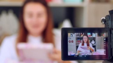Hediyeler paketleniyor. Çekici bir kadın, hediye ve dekorasyon tasarımcısı çevrimiçi eğitim programları, video bloğunu kaydediyor, giyim kuşamını takıyor, akıllı telefonun ve kameranın önünde oturuyor. çevrimiçi satış.