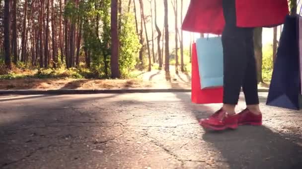 Donna con borse della spesa. gambe femminili in scarpe rosse, primo piano. Donna con borse colorate in mano, passeggiando per il parco cittadino. shopping e regali. concetto di consegna o donazione. — Video Stock