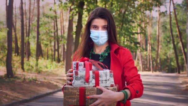 Regalos envueltos. una mujer con una máscara protectora sosteniendo varias cajas bellamente embaladas en sus manos. al aire libre. entrega o donación, concepto de caridad. regalos para las vacaciones — Vídeo de stock