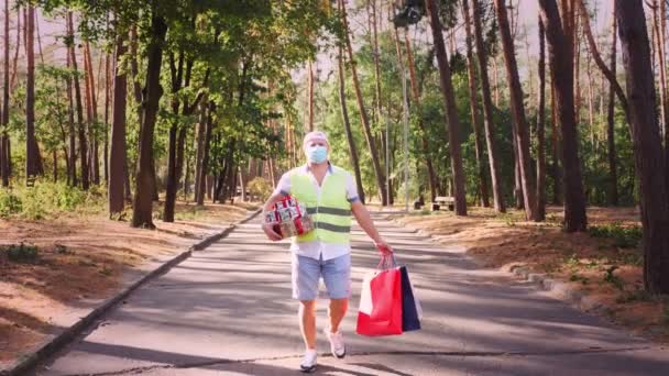 Man, koerier, met een beschermend masker, met verschillende geschenkdozen en boodschappentassen in zijn handen. Buiten. levering van geschenken voor party event. donatie, liefdadigheidsconcept — Stockvideo