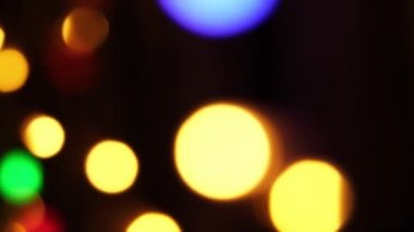 Soyut sahte arkaplan hareket halinde. Parlak, bulanık renkli parçacıklar, ışıklar. Koyu arkaplandaki çelenklerden parlak bir bokeh. Yeni yıl ya da Noel arkaplanı.