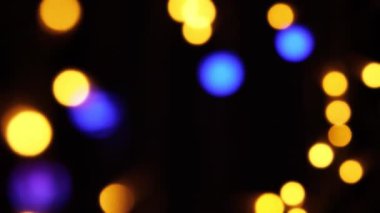 Soyut sahte arkaplan hareket halinde. Parlak, bulanık renkli parçacıklar, ışıklar. Koyu arkaplandaki çelenklerden parlak bir bokeh. Yeni yıl ya da Noel arkaplanı.