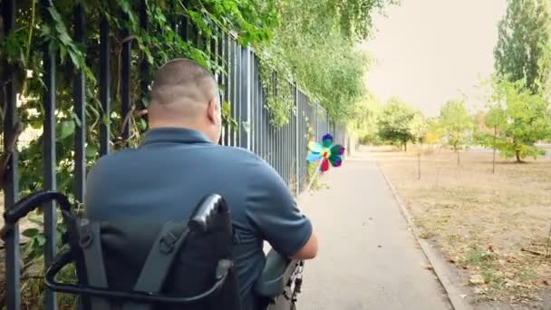 Rollstuhlfahrer. Behinderter Mann. Ein junger behinderter Mann im Rollstuhl fährt auf dem Gehweg am Zaun entlang. zurück — Stockvideo