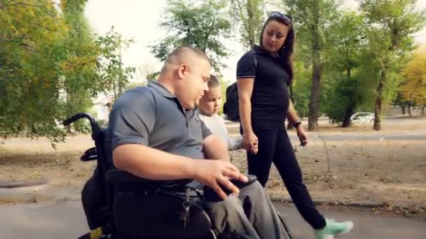 휠체어 남자. 장애인 이야. 자동 휠체어를 타고 화창 한 가을 날 가족, 아내, 어린아이들과 함께 도시 골목을 걷고 있는 장애인 청년. — 비디오
