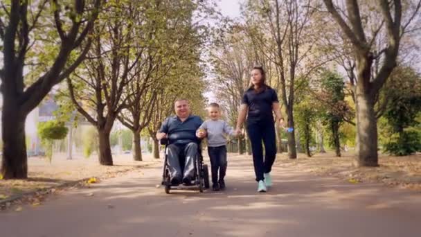 휠체어 남자. 장애인 이야. 자동 휠체어를 타고 화창 한 가을 날 가족, 아내, 어린아이들과 함께 도시 골목을 걷고 있는 장애인 청년. — 비디오