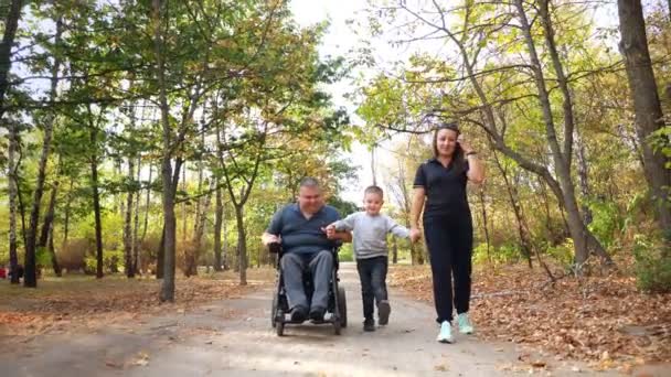 車椅子の男。ハンディキャップの男。自動運転車椅子の若い障害者は家族や妻や小さな子供と公園の晴れた秋の日に. — ストック動画