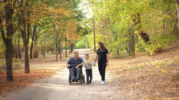 Wheelchair man. Handicapped man. young disabled man in an automated wheelchair walks with his family, wife and small child, in the park, on sunny autumn day. — Stock Video