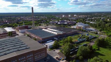 Endüstriyel binaların havadan görünüşü ve Almanya 'nın Hennigsdorf şehrinde bir bacanın yanından geçen bir tren. geniş yörünge görünümü dronu 