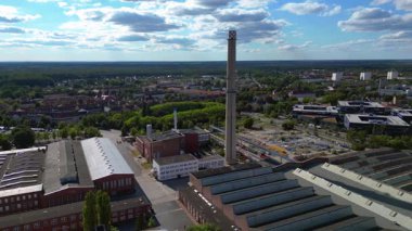 Endüstriyel binaların havadan görünüşü ve Almanya 'nın Hennigsdorf şehrinde bir bacanın yanından geçen bir tren. Yukarıdan drone atışı 