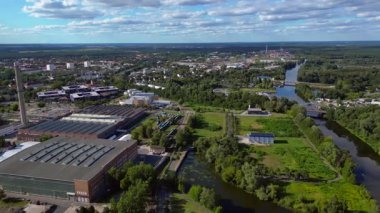 Endüstriyel binaların havadan görünüşü ve Almanya 'nın Hennigsdorf şehrinde bir bacanın yanından geçen bir tren. panorama genel görünüm dronu 