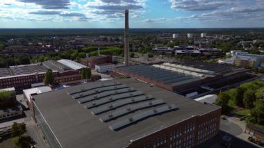 Endüstriyel binaların havadan görünüşü ve Almanya 'nın Hennigsdorf şehrinde bir bacanın yanından geçen bir tren. Ters İHA uçuşu 