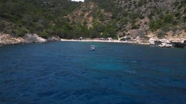 Ibiza 'da bazı balıkçıların evlerinin olduğu gizli bir sahil koyunun yakınında sakin mavi sularda yüzen yelkenli. İHA yükseliyor 