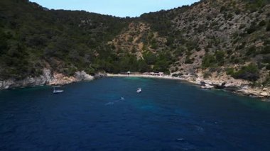 Ibiza 'da bazı balıkçıların evlerinin olduğu gizli bir sahil koyunun yakınında sakin mavi sularda yüzen yelkenli. İticileri ileri çalıştır 