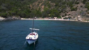 Ibiza 'da bazı balıkçıların evlerinin olduğu gizli bir sahil koyunun yakınında sakin mavi sularda yüzen yelkenli. Ters İHA uçuşu 