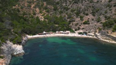 Yazın İspanya 'nın İbiza kentindeki güzel Cala Llentrisca sahilinin turkuaz suyu ve Barques de Pescadors Huts manzarası. panorama genel görünüm dronu 