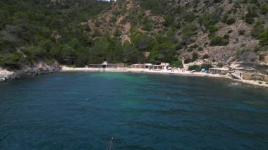 Ibiza 'da bazı balıkçıların evlerinin olduğu gizli bir sahil koyunun yakınında sakin mavi sularda yüzen yelkenli. Üstten uçan uçak ters uçuyor. 