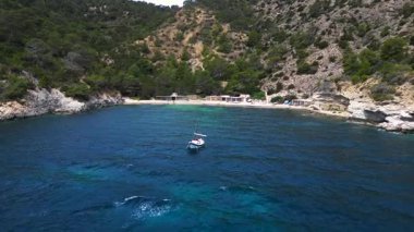 Ibiza 'da bazı balıkçıların evlerinin olduğu gizli bir sahil koyunun yakınında sakin mavi sularda yüzen yelkenli. Uçarken üstten uçmak İHA 'yı ileri itmek 