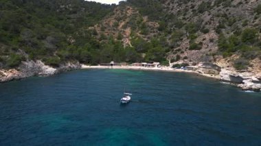 Ibiza 'da bazı balıkçıların evlerinin olduğu gizli bir sahil koyunun yakınında sakin mavi sularda yüzen yelkenli. uçuş üstü insansız hava aracı 